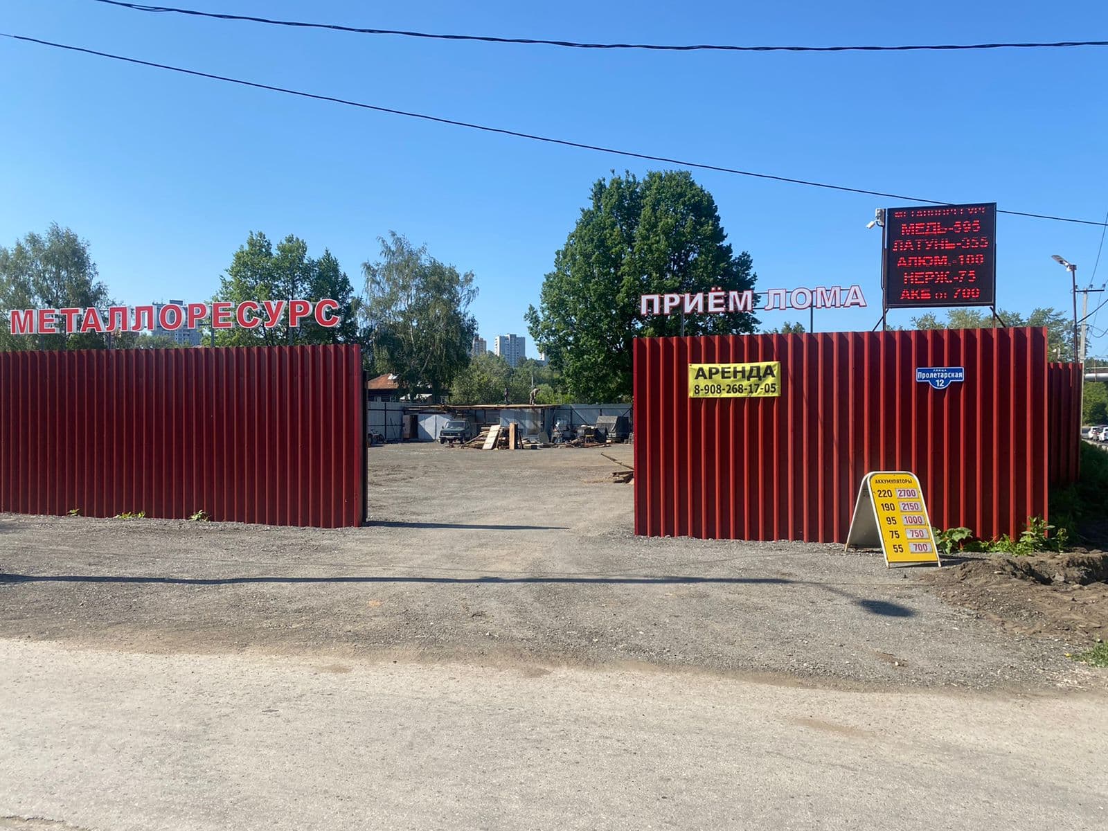 Въезд в Металлоресурс: красный металлический забор и вывеска Приём лома